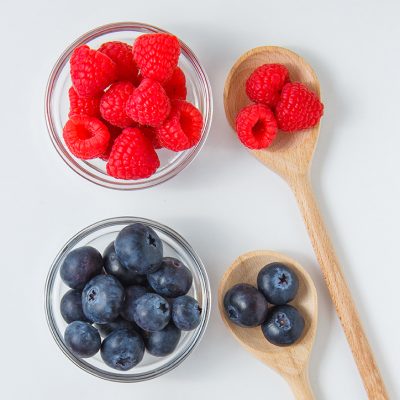 Set of blueberries and raspberries in a spoons and saucers on a white background. top view.