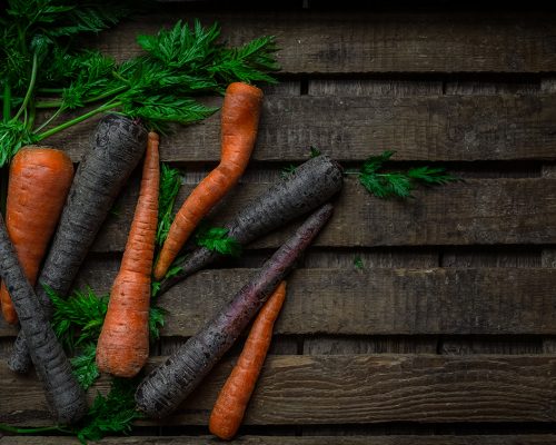 Purple and orange carrots, green stems in wooden crate, top view. Horizontal image with copy space
