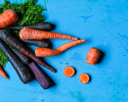 Orange and purple carrots on grunge blue background, top view. Horizontal image with copy space